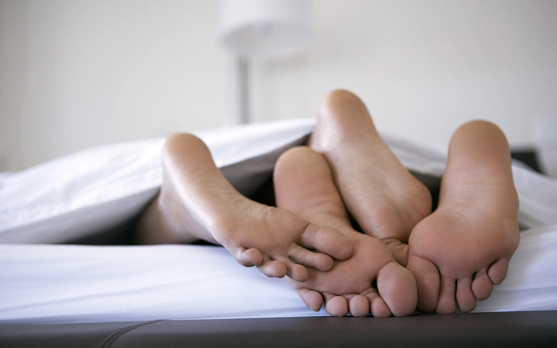 Контакт в постели. Мужские и женские ступни. Ноги на кровати. Пятки под одеялом. Мужские и женские ноги в кровати.